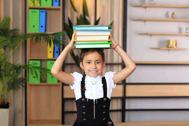 Egy iskolai egyenruhás lány portréja könyvekkel a fején.. - Fotó, kép
