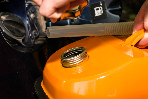 Egy férfi kezében egy narancssárga benzines kanna a kocsi mellett, kihúzza a dugót a töltőanyag nyakából. Kiváló minőségű fénykép - Fotó, kép
