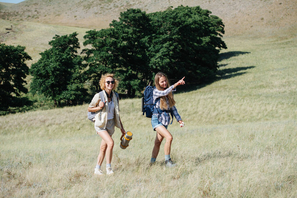 Cheerful women friends hiking in grassy hills, going uphill, talking. Pointing at a distance. - Fotó, kép