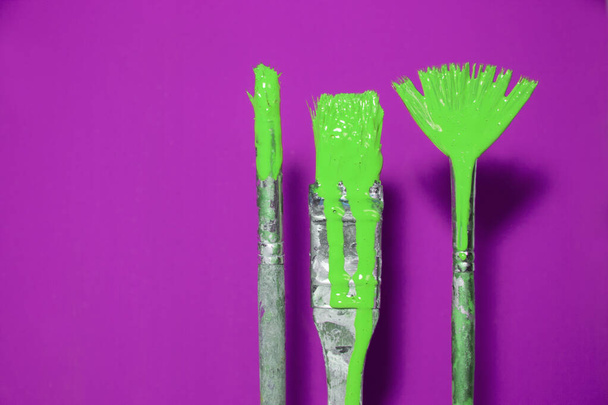 Variety of brushes with dripping green paint on a vibrant blue background. - Photo, image