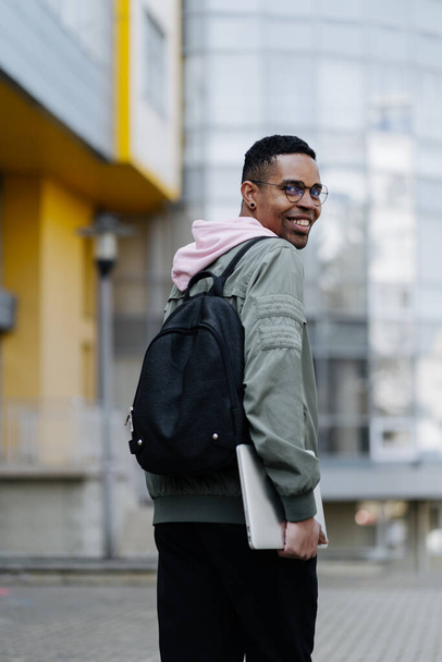 Young man wearing jaket and backpack outdoors holding laptop - Photo, image
