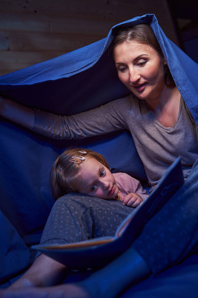 Parent with kid with book covering themselves with blanket - Foto, Bild