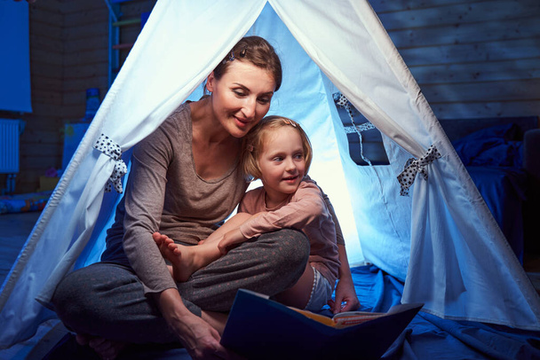 Mother and daughter sitting in tent in bedroom - Фото, изображение