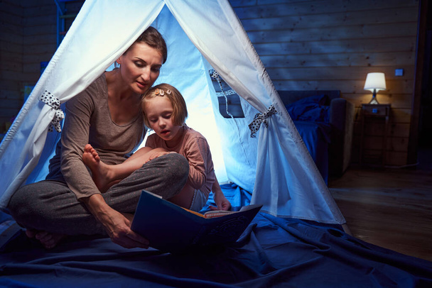 Adult and child in a tent at home reading book - 写真・画像