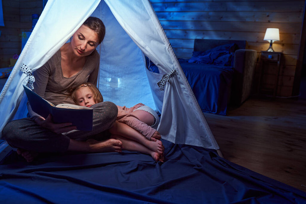 Mother with storybook helping her daughter to fall asleep - Foto, Bild