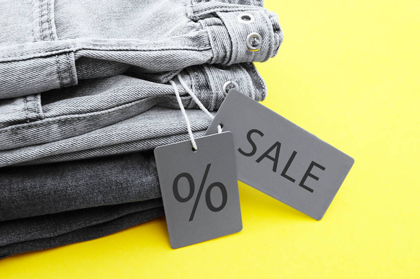 Detail černých džínů, šedých štítků a nápisu Prodej na žlutém pozadí. Nákupní a slevový koncept. Černý pátek. - Fotografie, Obrázek