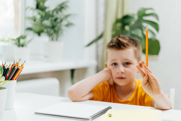Distance learning online education. Caucasian smile kid boy studying at home with book, writing in notepad and doing school homework. Thinking child siting at table with notebook. Back to school - Valokuva, kuva