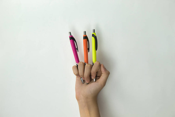 χέρι κοριτσιού που κρατά τρεις πένες διαφορετικού χρώματος μεταξύ των δακτύλων σε λευκό φόντο - Φωτογραφία, εικόνα