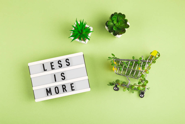 Less is more - scritto su lightbox accanto al carrello intrecciato con piante e piante grasse in vasi su sfondo verde. - Foto, immagini