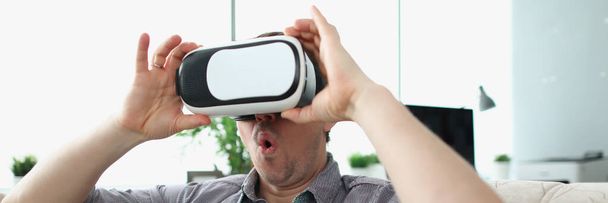 Surprised man wearing virtual reality glasses sitting on couch at home - Photo, Image