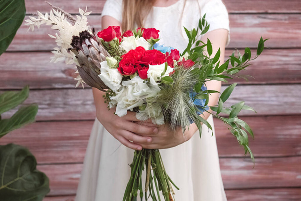 Beautiful girl in a green dress holding a bouquet of flowers and greenery on a wooden background. Copy, empty space for text - Фото, зображення
