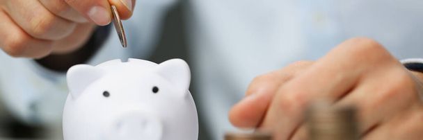 Man hand putting coin into white piggy bank closeup - Photo, Image