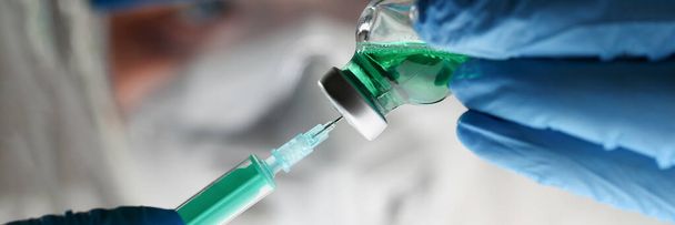 Az orvos védőöltözetben és kesztyűben gyógyszert visz az injekciós üvegből a fecskendőbe. - Fotó, kép