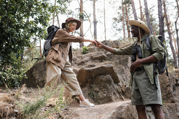 Afrika kökenli Amerikalı yürüyüşçü ormanda kıdemli eşinin elini tutuyor.  - Fotoğraf, Görsel