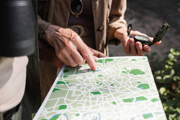 Ausgeschnittene Ansicht einer Seniorin mit Kompass, der auf eine Karte in der Nähe eines afrikanisch-amerikanischen Ehemannes zeigt  - Foto, Bild