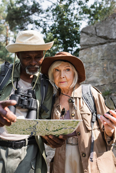 Старшие мультиэтнические туристы с компасом и картой, стоящие в лесу  - Фото, изображение