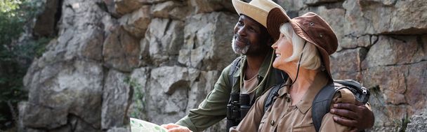 Senior african american hiker hugging smiling wife with map near rock, banner  - Foto, Imagen