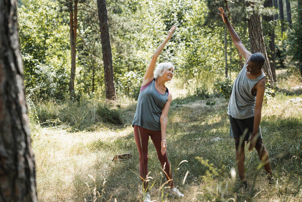 Літня багатонаціональна пара розігрівається в лісі
  - Фото, зображення