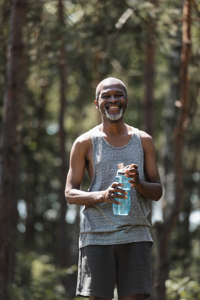 Senior african american sportsman holding sports bottle in summer forest  - Photo, Image
