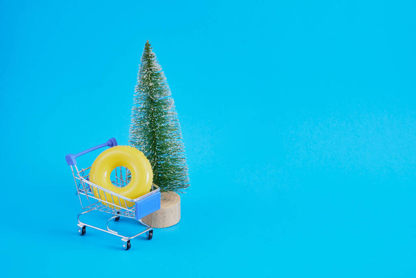 toy decorative Christmas tree, an inflatable circle in a shopping cart on a blue background. Celebrate new year on the seaside, winter holidays on the beach - Fotoğraf, Görsel