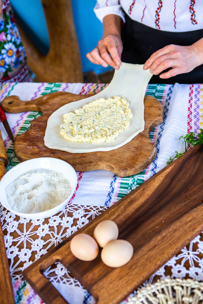 image avec les mains d'une dame cuisinant des tartes roumaines traditionnelles avec du fromage dans des vêtements traditionnels. - Photo, image