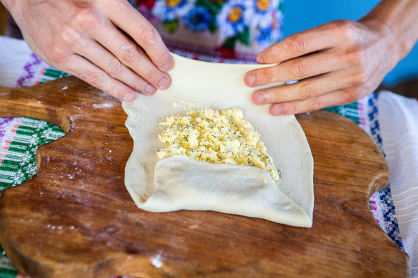 beeld met de handen van een dame koken traditionele Roemeense gebakken taarten met kaas in traditionele kleren. - Foto, afbeelding