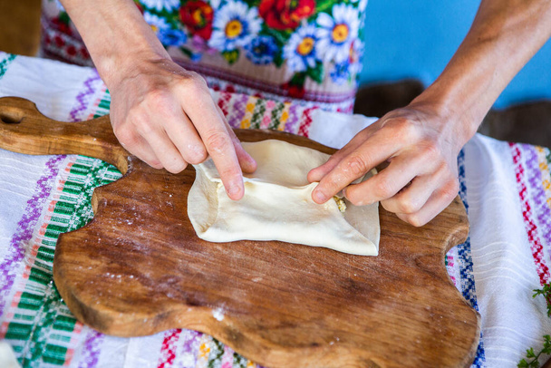 Bild mit den Händen einer Dame, die traditionelle rumänische frittierte Kuchen mit Käse in traditioneller Kleidung kocht. - Foto, Bild