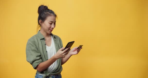 Szépség vonzó ázsiai fiatalok elszigetelt hölgy élvezze telefon görgetés e-shop és hitelkártya vásárlás online bolt a siker fizetési sárga háttér. Készíts másolási helyet. A betéti kártya koncepciója. - Felvétel, videó