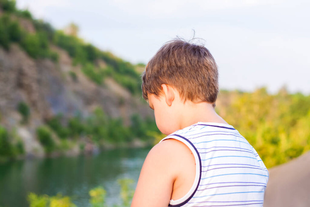 子供は美しい渓谷の上に座って、そこの水を見ています。渓谷の岸だ。子の肖像. - 写真・画像