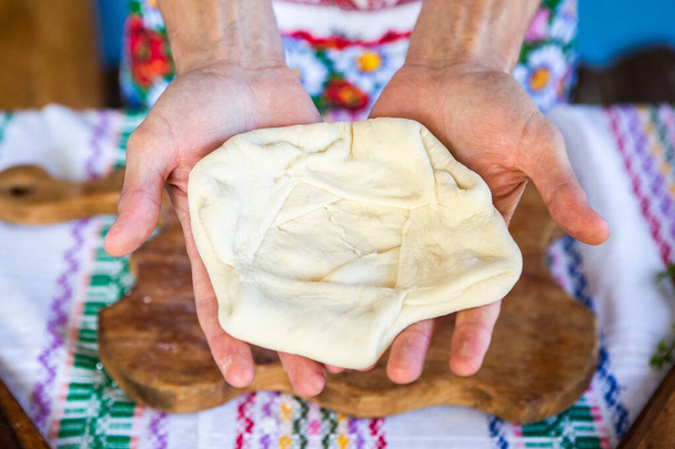 з руками жінки, яка готує традиційний румунський смажений пиріг з сиром в традиційному одязі.. - Фото, зображення