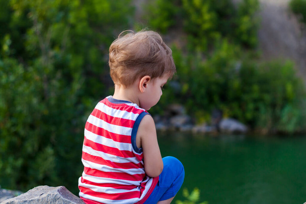 A child sits on the top of a beautiful canyon and looks at the water in it. The bank of the canyon. Portrait of a child. - 写真・画像