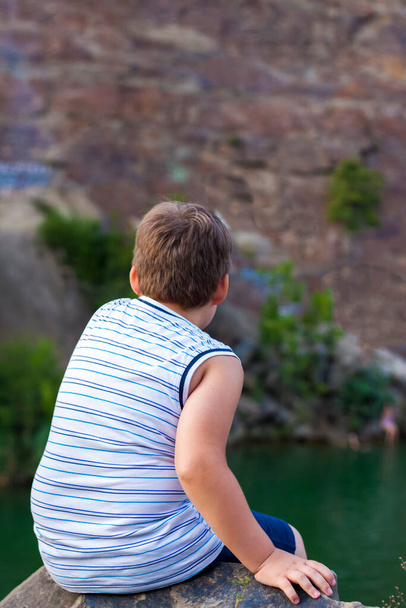 A child sits on the top of a beautiful canyon and looks at the water in it. The bank of the canyon. Portrait of a child. - Photo, image