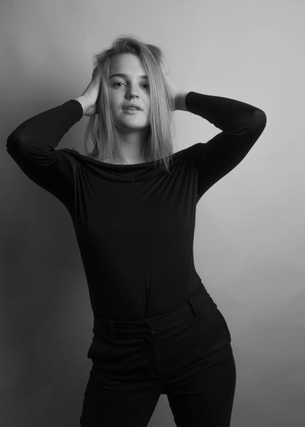Girl, blonde, shoulder-length hair. Posing in the studio on a light background. Black clothes. Spring summer type. Baby face. Black and white photo - Photo, Image