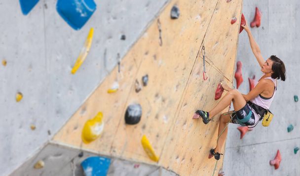 la chica sube a la pared de escalada. escalada en roca como un tipo de recreación activa en la ciudad. practicar deportes en la naturaleza - Foto, imagen