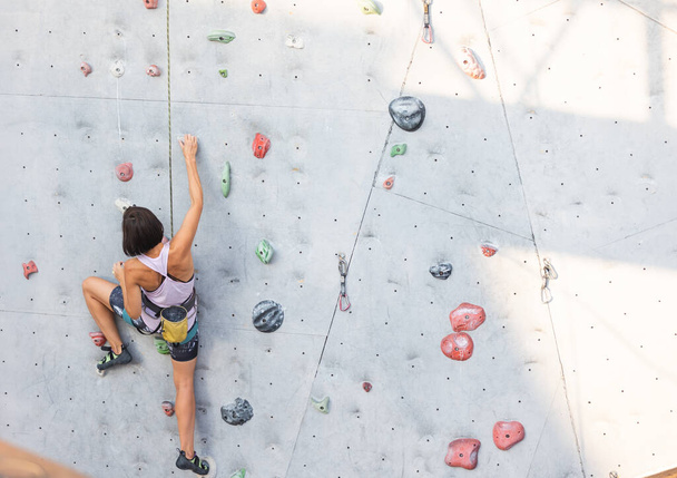 Dziewczyna wspina się na ścianę wspinaczkową. wspinaczka skalna jako rodzaj aktywnego wypoczynku w mieście. uprawianie sportu w przyrodzie - Zdjęcie, obraz