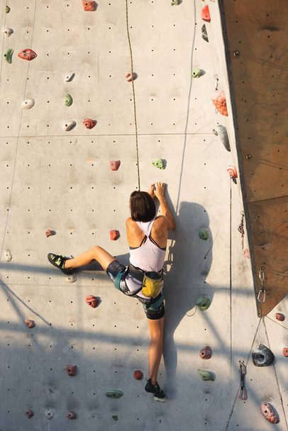 девушка лезет на стену для скалолазания. скалолазание как вид активного отдыха в городе. спорт на природе - Фото, изображение
