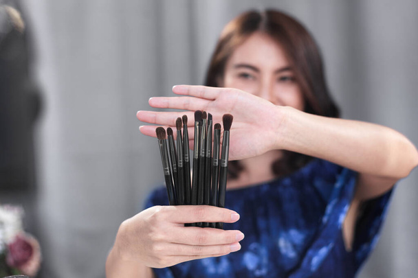Blogueuse beauté asiatique enregistrant un guide facile pour les débutants de pinceaux cosmétiques avec des produits de maquillage et le partage sur les médias sociaux en ligne avec un appareil photo numérique à la maison. Focus sélectif sur les brosses - Photo, image