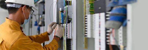 Villamosmérnök, aki digitális multiméter vizsgálati áramot használ a vezérlőpanelben elektromos berendezések és vezetékek vizsgálatára az új épületen lévő gépházban.. - Fotó, kép