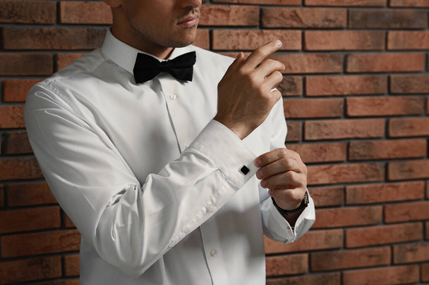 Stylish man putting on cufflink near brick wall, closeup - Photo, image