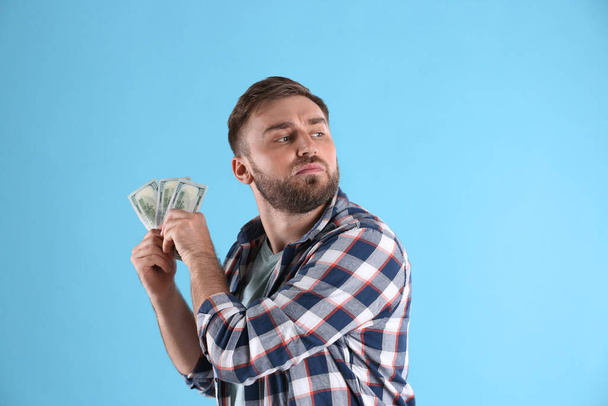 Greedy young man hiding money on light blue background - Foto, Imagem