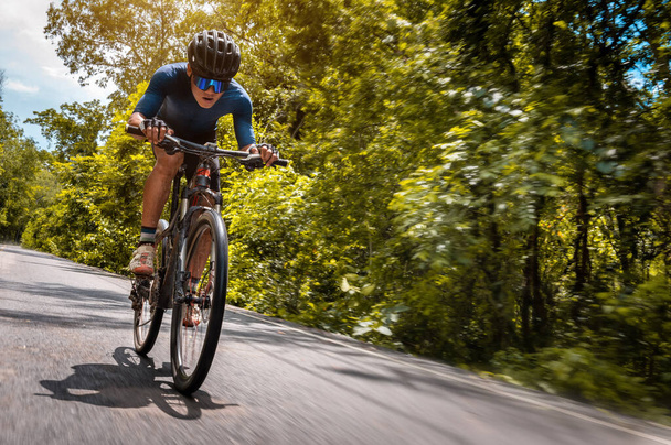 Велогонка, велосипедист на скоростном горном велосипеде по дороге со стороны леса. Занятия спортом на свежем воздухе доставляют удовольствие. Основные методики тренировки по следу спортсменов. Сосредоточиться на велосипедисте - Фото, изображение