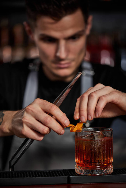 bartender makes a cocktail in a glass with orange peel - Fotoğraf, Görsel