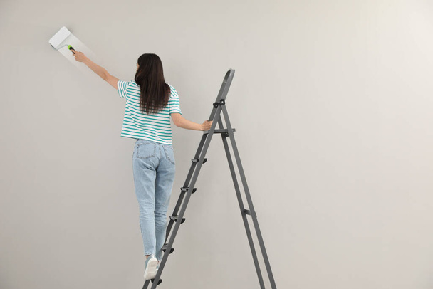 Молодая женщина роспись стены с роликом на лестнице, вид сзади - Фото, изображение