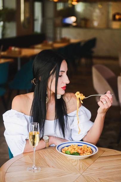 Gorgeous young brunette woman having Italian food. Beautiful woman inside Italian restaurant eating traditional Italian pasta spaghetti. Alone in restaurant, social distancing. Fashion shooting. - Photo, image