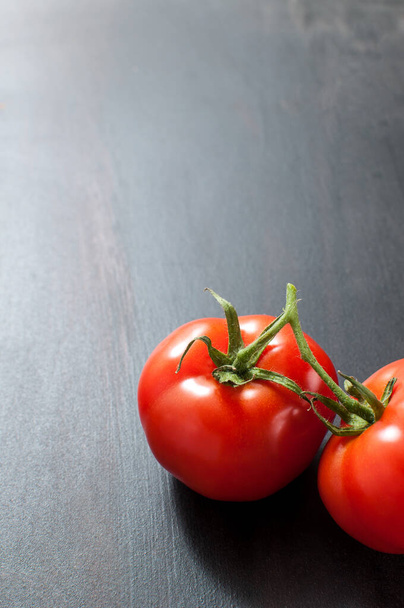 Koyu gri arkaplanda iki taze organik domates, kopyalanmış dikey görüntü - Fotoğraf, Görsel