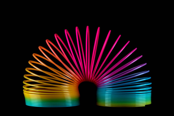 Colourful slinky spring toy isolated on a black background - Foto, afbeelding