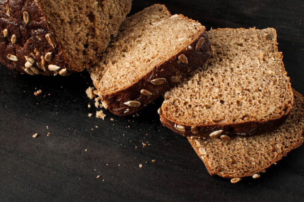 Close up of a delicious fresh baked slices of bread with sunflower seeds on a dark table, horizontal image - Foto, Bild