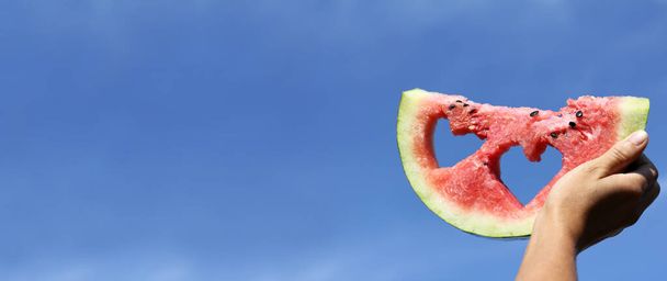 red slice of watermelon with holes in the shape of hearts against the blue sky. favorite season is summer - Foto, Imagem