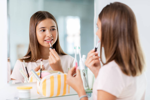teenage girl applying lip gloss at bathroom - Zdjęcie, obraz