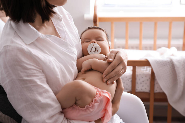 Mother holding her cute little baby with pacifier at home, closeup - Фото, зображення
